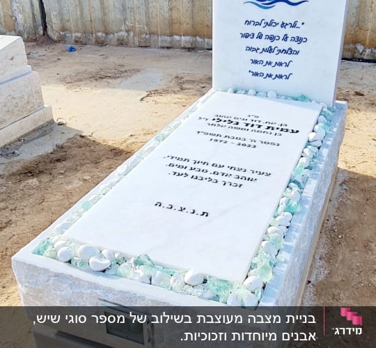 מצבה לבנה עם כיתוב בעברית ואבנים מסביב